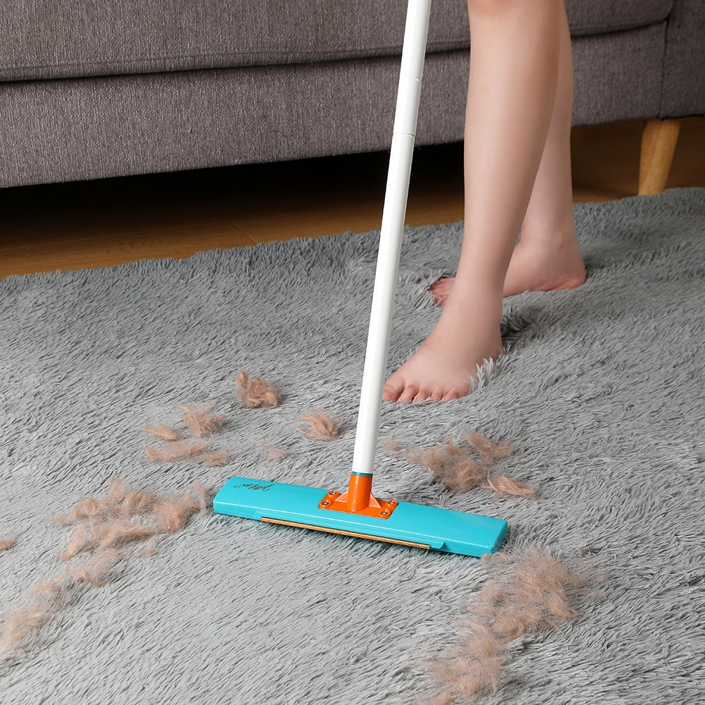 Steel pin brush side of the Jolllax Carpet Rake removing embedded pet hair from medium-pile carpet.
